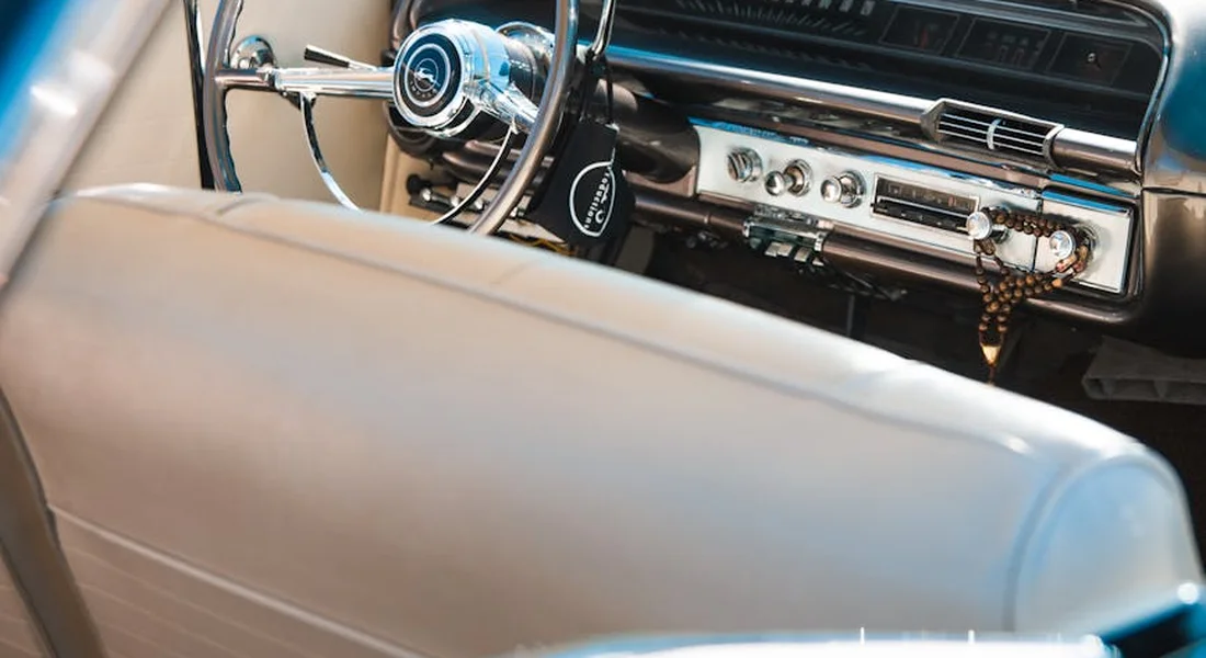 Close-up of a vintage car's dashboard and steering wheel with light-colored upholstery in the foreground.
