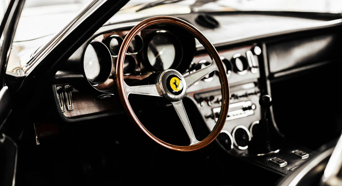 Close-up of a classic car interior featuring a wooden steering wheel and chrome dashboard controls.