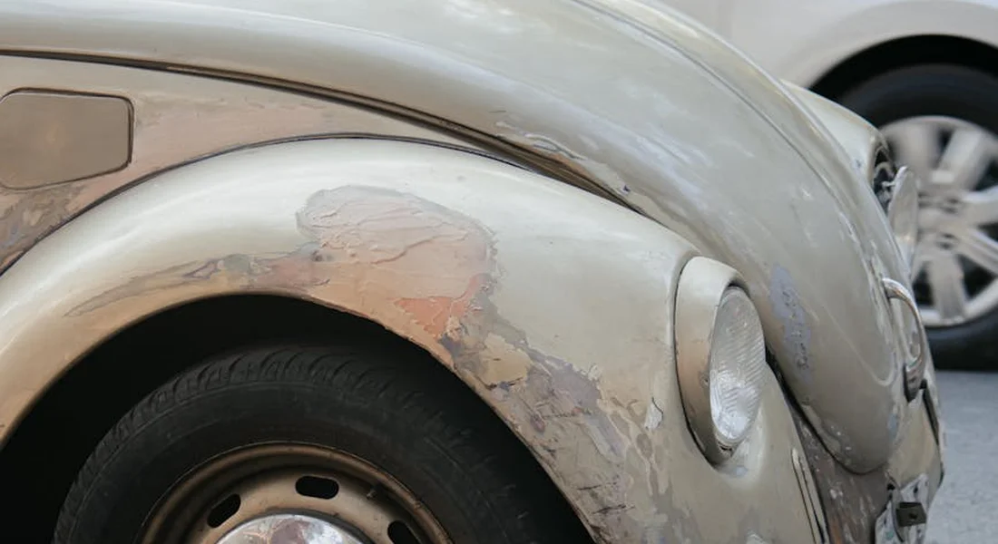 Close-up of a vintage car fender with peeling and chipped beige paint.
