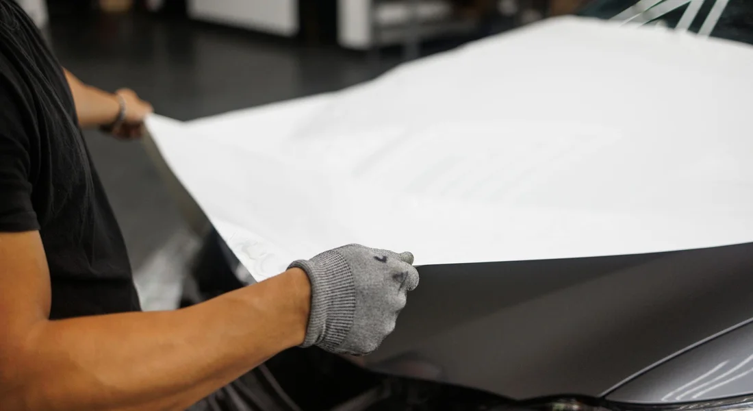 Technician wearing gloves applies a vinyl wrap to the hood of a car