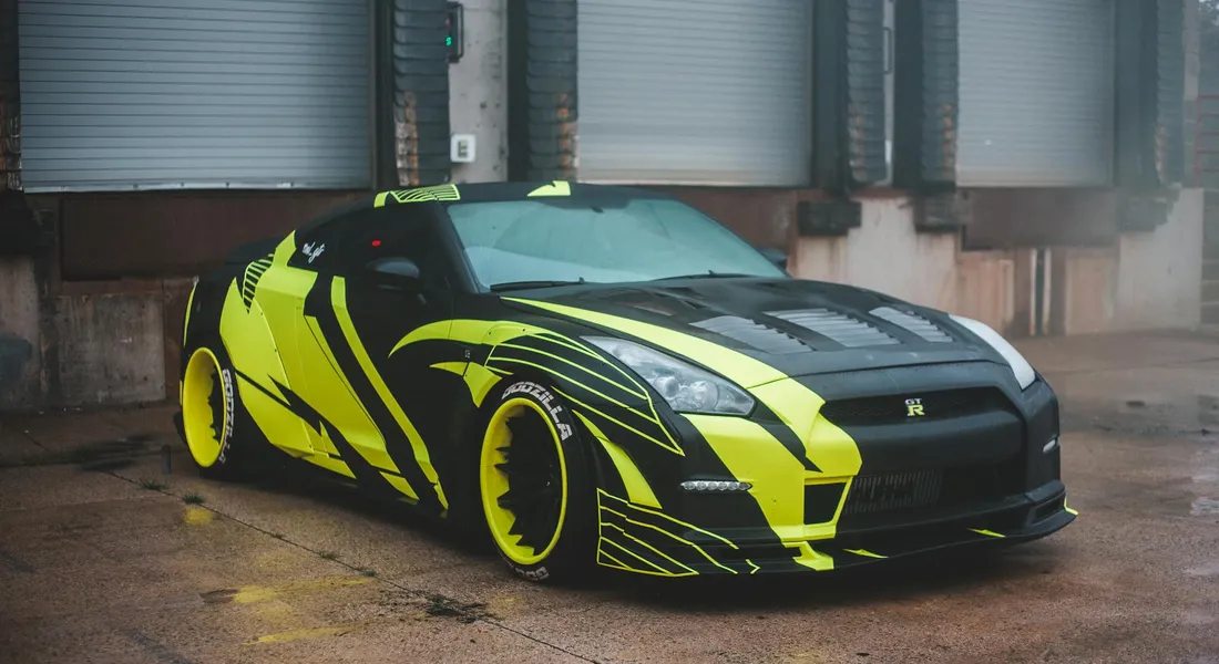 Neon-yellow and black vinyl wrap on a sports car parked near an industrial building.
