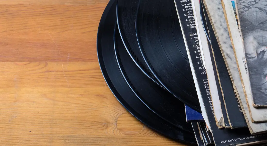 Close-up of vinyl records stacked on a warm wooden surface.