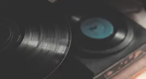 Close-up view of a vinyl record with visible grooves on a turntable, a blue record label in the background.