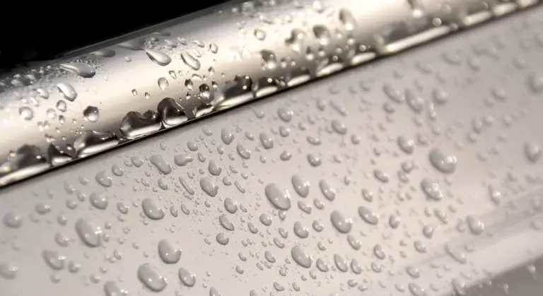 Close-up of water droplets on a car's paint surface, showing spots and marks on the finish.