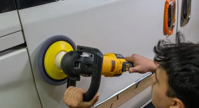 Technician using a yellow-pad polisher to wet-sand the clear coat on a car's door panel.