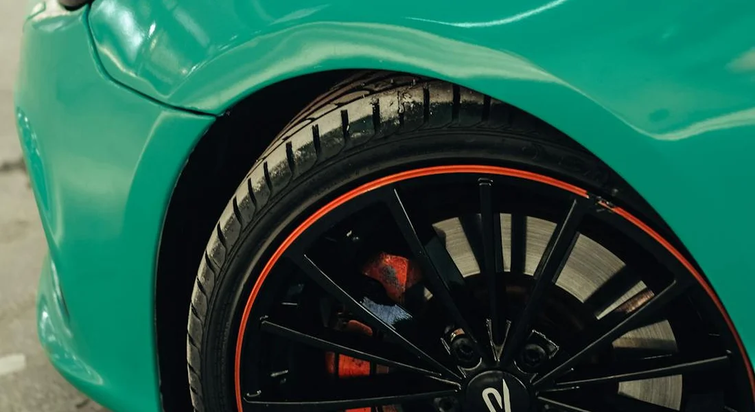 Close-up of a bright green car body and black alloy wheel with an orange rim, showcasing a smooth, reflective paint finish.