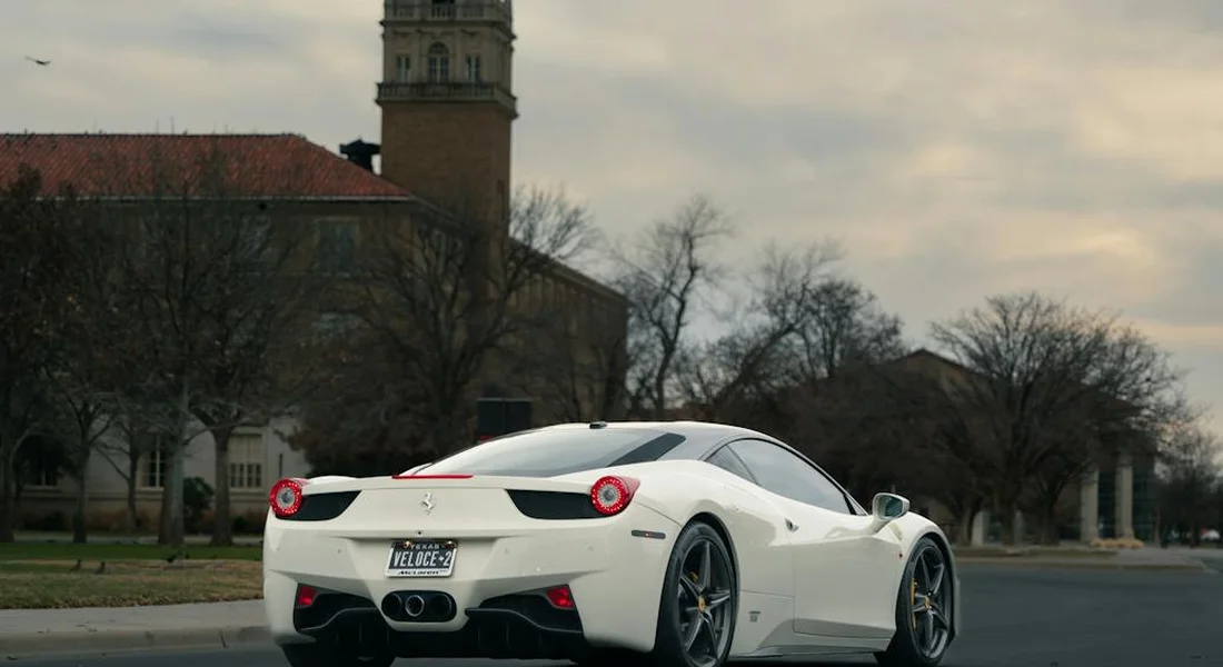 White luxury sports car parked on a street with a historic building and bare trees in the background.