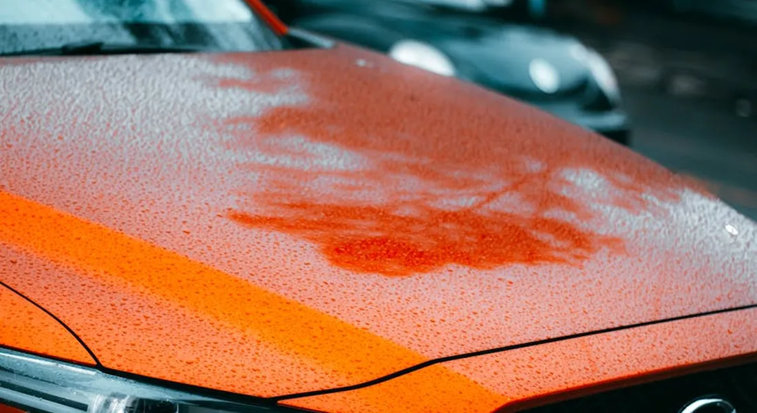 Close-up of an orange car hood with water spots and droplets