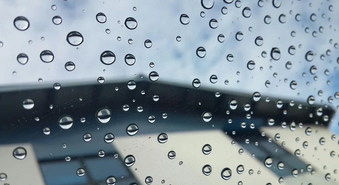 Close-up of water droplets on a car windshield with a blurred background, illustrating precision in glass polishing.