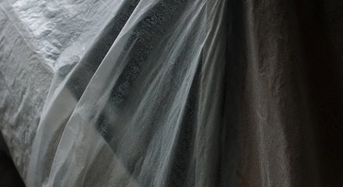 Close-up of translucent protective fabric draped in a garage, suggesting a car cover used to shield paint in winter.