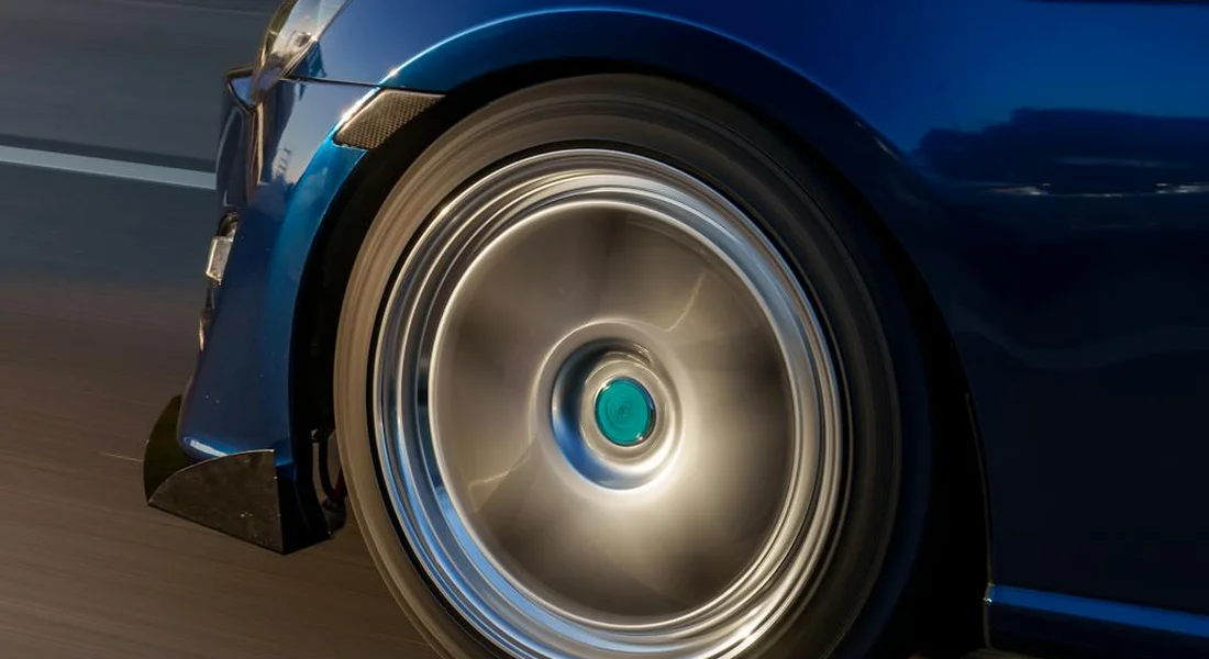 Close-up of a blue wrapped car's front wheel with a polished rim, motion blur on the road