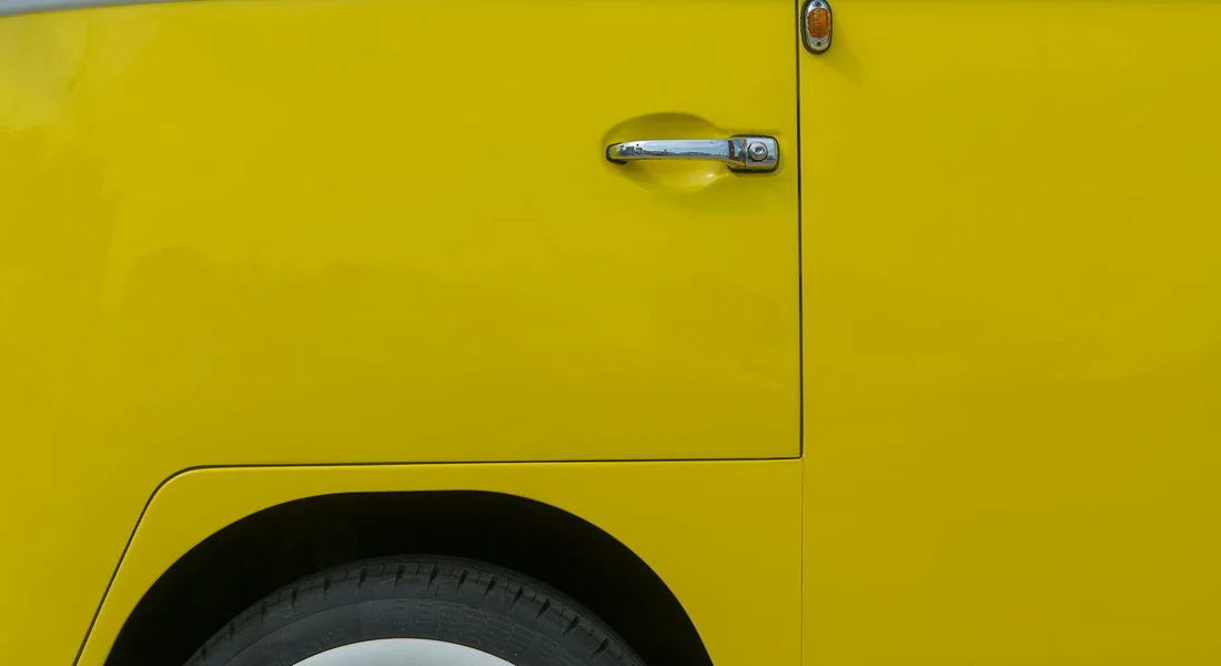 Close-up of a bright yellow van door and wheel, illustrating color-matching challenges in vehicle detailing.